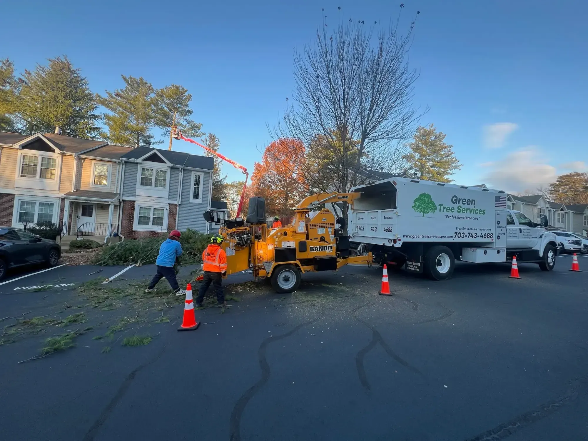 Crew feeding branches into a chipper beside a Green Tree Services truck
